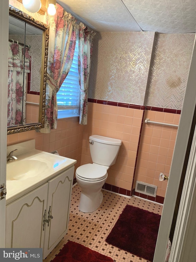 full bathroom featuring tile walls, wainscoting, toilet, wallpapered walls, and vanity