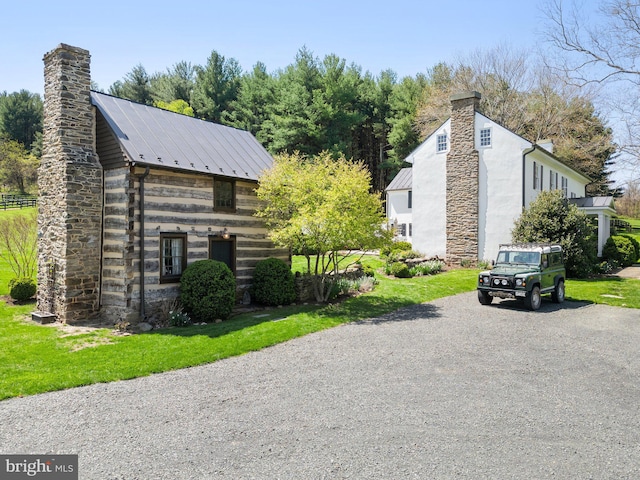 view of property exterior featuring a chimney, metal roof, gravel driveway, and a yard