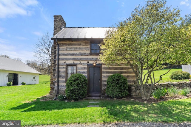 view of front of home featuring a chimney, a standing seam roof, a front yard, and metal roof