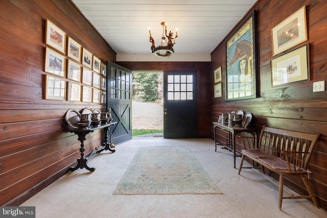 entrance foyer featuring wooden walls, carpet flooring, and a chandelier