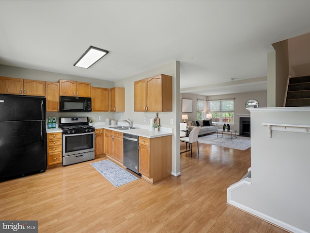 kitchen featuring light wood-style floors, open floor plan, light countertops, a sink, and black appliances
