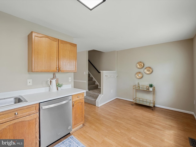 kitchen featuring light countertops, baseboards, stainless steel dishwasher, and light wood finished floors
