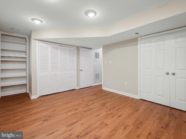 unfurnished bedroom with light wood-type flooring, baseboards, two closets, and visible vents