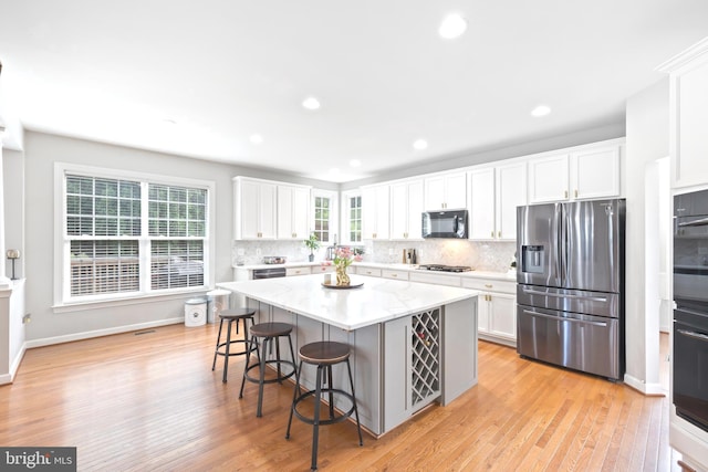 14401 Broadwinged Dr, Gainesville, VA 20155 - kitchen featuring black appliances, white cabinets, tasteful backsplash, a kitchen breakfast bar, and light wood-type flooring