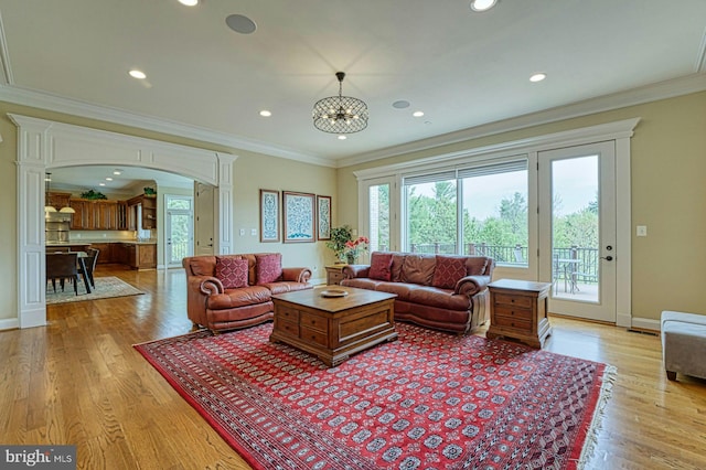 living area featuring arched walkways, crown molding, light wood finished floors, and recessed lighting