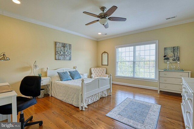 bedroom featuring baseboards, wood finished floors, visible vents, and ornamental molding