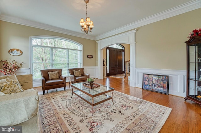 living room featuring arched walkways, crown molding, wainscoting, a chandelier, and a decorative wall