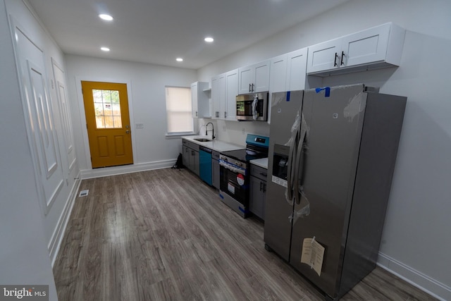 kitchen featuring appliances with stainless steel finishes, a sink, open shelves, wood finished floors, and white cabinetry