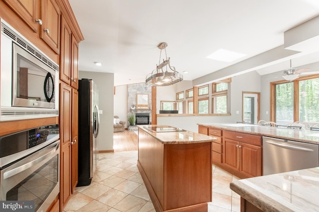 16 Hunters Ln, Chadds Ford, PA 19317 - kitchen with light stone countertops, a fireplace, brown cabinetry, stainless steel appliances, and a kitchen island