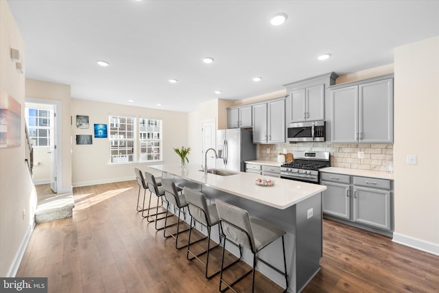 kitchen with a sink, appliances with stainless steel finishes, gray cabinetry, baseboards, and a kitchen bar
