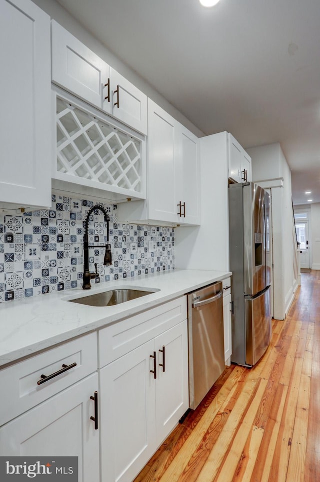 kitchen featuring tasteful backsplash, a sink, light wood-style flooring, white cabinets, and appliances with stainless steel finishes
