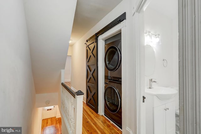 clothes washing area featuring a barn door, a sink, stacked washer / drying machine, light wood finished floors, and laundry area