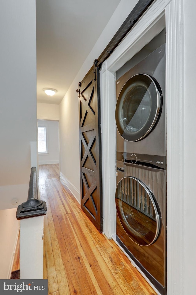 laundry room with a barn door, stacked washer / dryer, laundry area, baseboards, and hardwood / wood-style flooring