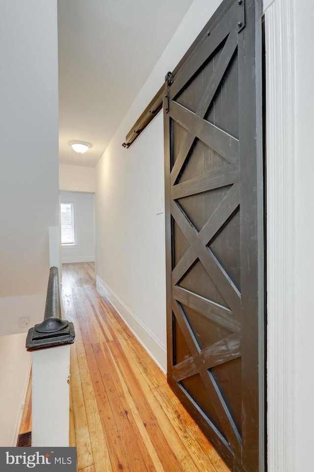 hall featuring a barn door, light wood-style floors, and baseboards
