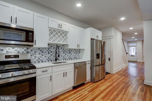 kitchen featuring stainless steel appliances, light countertops, a sink, decorative backsplash, and white cabinetry