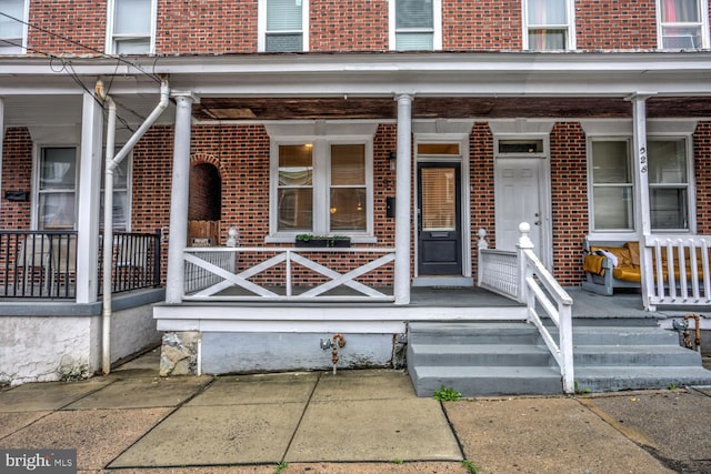 view of exterior entry featuring a porch and brick siding