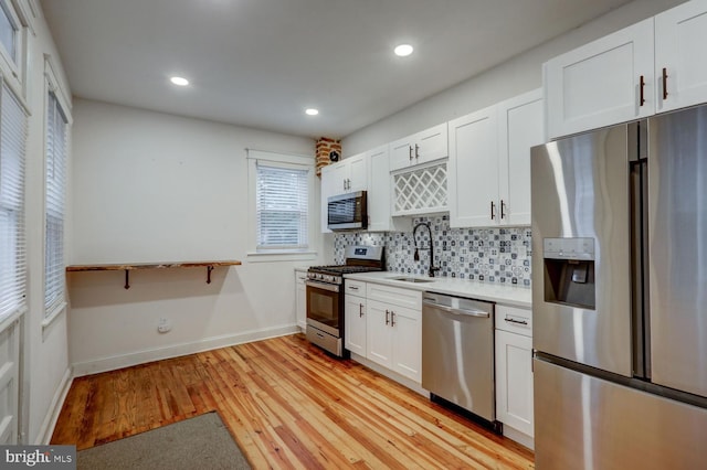 kitchen featuring stainless steel appliances, a sink, backsplash, white cabinetry, and light countertops