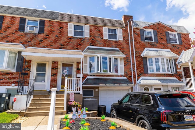 townhome / multi-family property with central AC unit, brick siding, cooling unit, and a garage