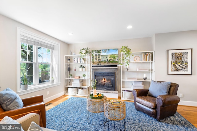 living area with a glass covered fireplace, recessed lighting, baseboards, wood finished floors, and visible vents