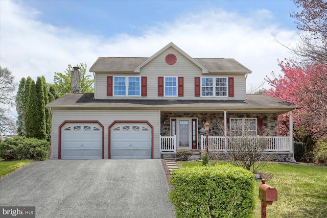 view of front of property featuring a front lawn, a chimney, covered porch, a garage, and aphalt driveway
