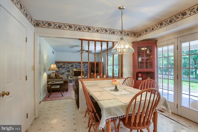 dining room featuring light floors, a fireplace, ceiling fan with notable chandelier, and plenty of natural light