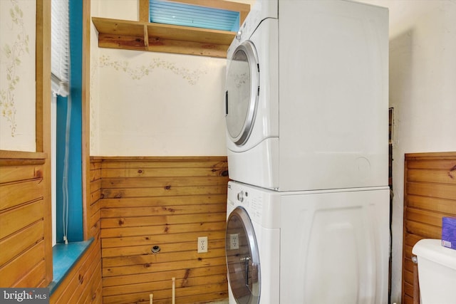 washroom featuring laundry area, wainscoting, stacked washer / drying machine, and wooden walls