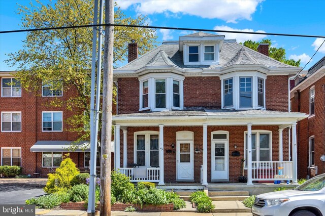 view of front of property featuring covered porch, a chimney, and brick siding