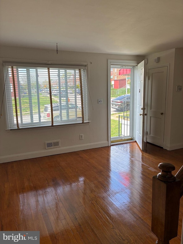 unfurnished living room with hardwood / wood-style flooring, a wealth of natural light, visible vents, and baseboards