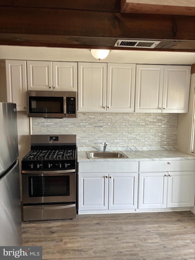 kitchen with white cabinets, stainless steel appliances, light wood-style flooring, a sink, and backsplash