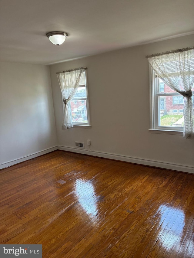 unfurnished room featuring wood-type flooring, visible vents, and baseboards
