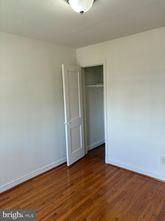 unfurnished bedroom featuring baseboards, dark wood-type flooring, and a closet
