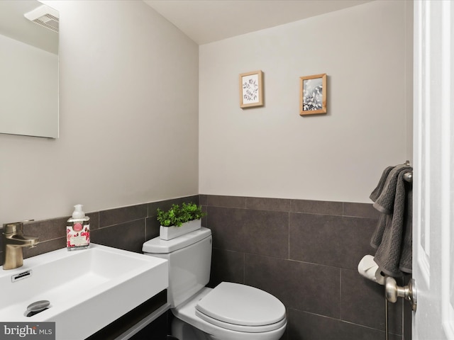 half bathroom with wainscoting, vanity, toilet, tile walls, and visible vents