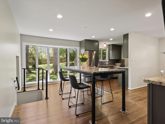 kitchen with baseboards, light stone countertops, a kitchen bar, and high end fridge