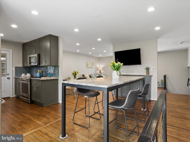 kitchen featuring light stone countertops, dark wood finished floors, stainless steel appliances, recessed lighting, and decorative backsplash