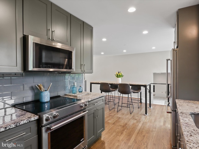 kitchen with tasteful backsplash, light wood-type flooring, light stone counters, stainless steel appliances, and recessed lighting
