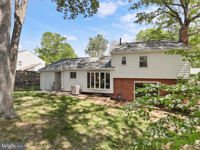 back of house with fence, a chimney, brick siding, a lawn, and central air condition unit