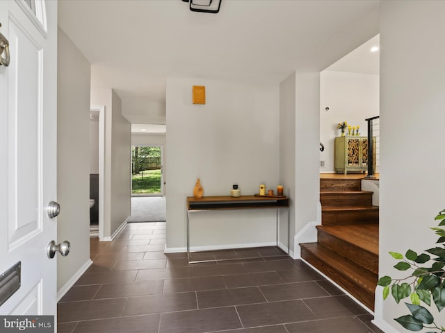 foyer featuring stairway, baseboards, and dark tile patterned flooring