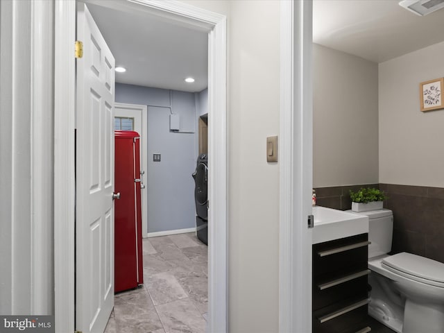 half bathroom with vanity, toilet, marble finish floor, tile walls, and visible vents
