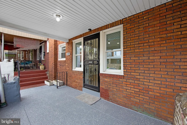 view of exterior entry featuring brick siding and covered porch