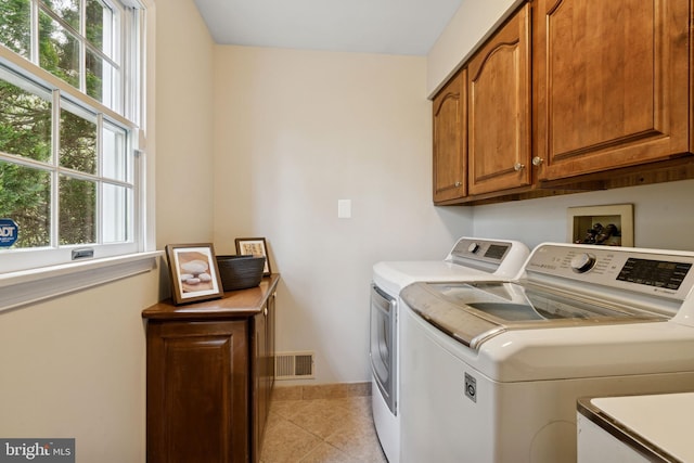 washroom with visible vents, light tile patterned floors, washing machine and dryer, baseboards, and cabinet space