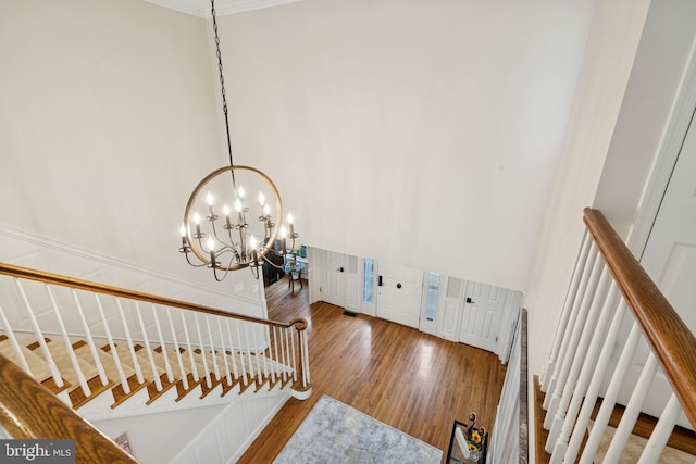 staircase featuring an inviting chandelier, crown molding, wood finished floors, and a towering ceiling
