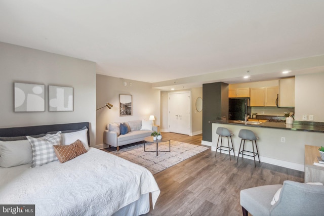 bedroom featuring a sink, baseboards, freestanding refrigerator, recessed lighting, and wood finished floors