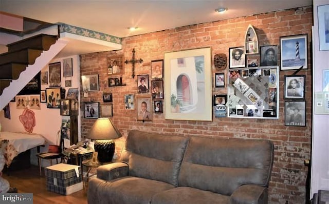 living area with wood finished floors, stairs, and brick wall