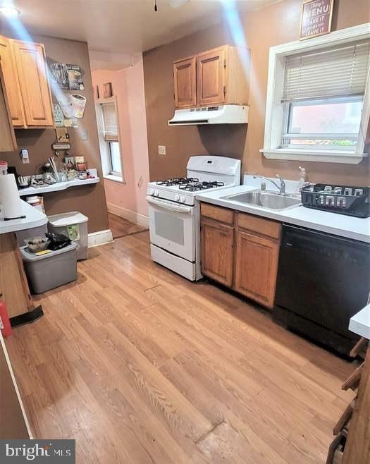 kitchen featuring under cabinet range hood, dishwasher, a sink, light wood-type flooring, and white range with gas cooktop