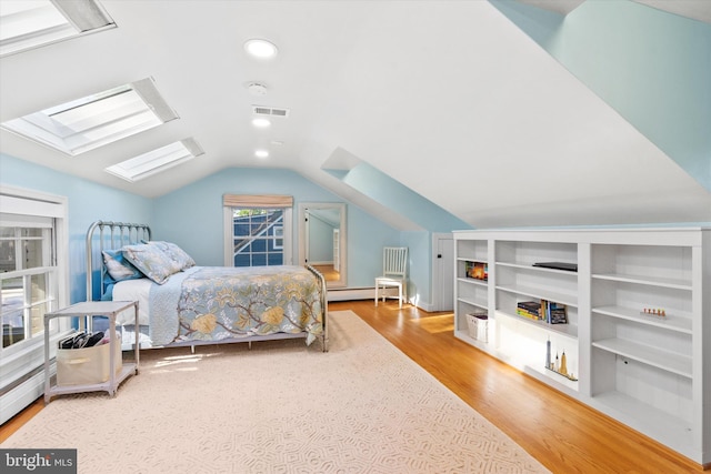 bedroom with lofted ceiling with skylight, visible vents, wood finished floors, and a baseboard radiator