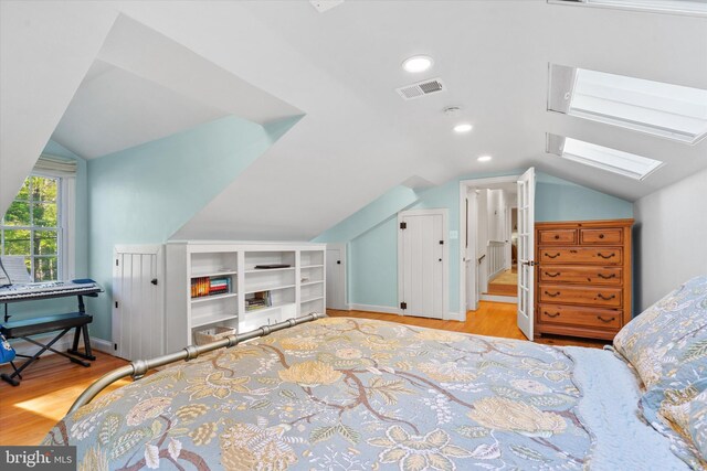 bedroom with lofted ceiling with skylight, visible vents, and wood finished floors