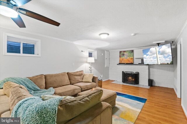 living area featuring wood finished floors, ornamental molding, ceiling fan, a brick fireplace, and baseboards