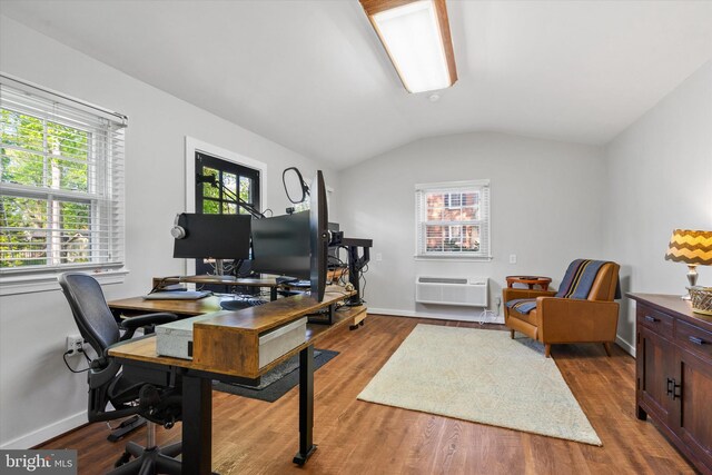 home office with lofted ceiling, a wall unit AC, wood finished floors, and baseboards