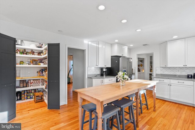 kitchen with white cabinets, stainless steel refrigerator with ice dispenser, and decorative backsplash