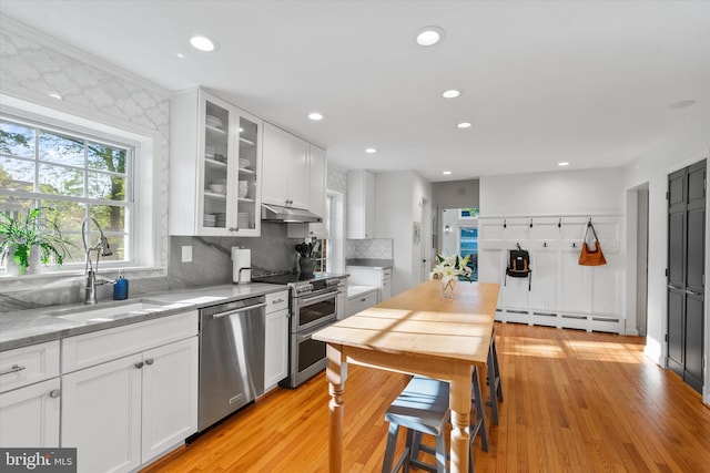 kitchen featuring white cabinetry, tasteful backsplash, stainless steel appliances, baseboard heating, and under cabinet range hood